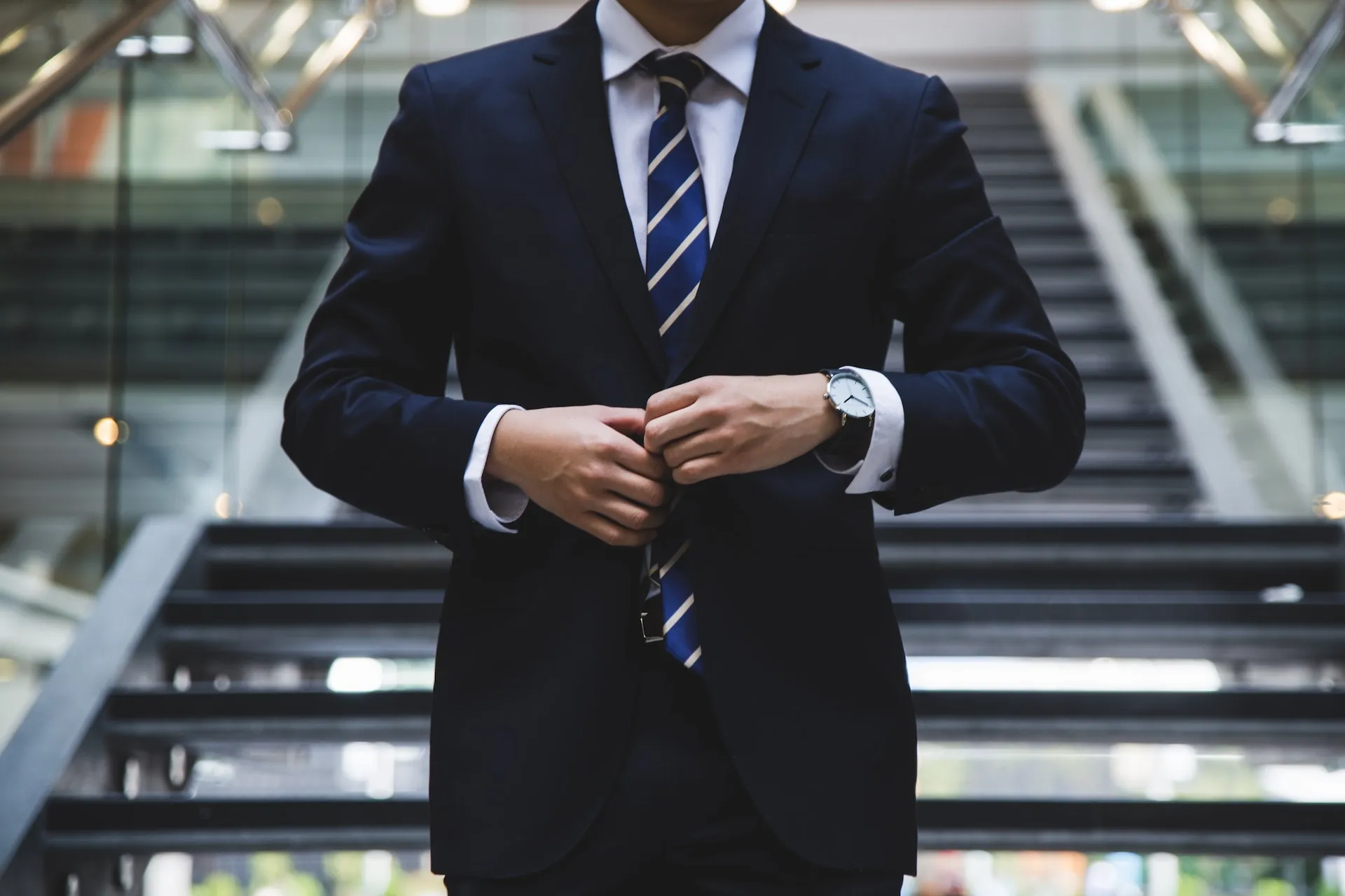 A business person buttoning up their jacket in front of a staircase