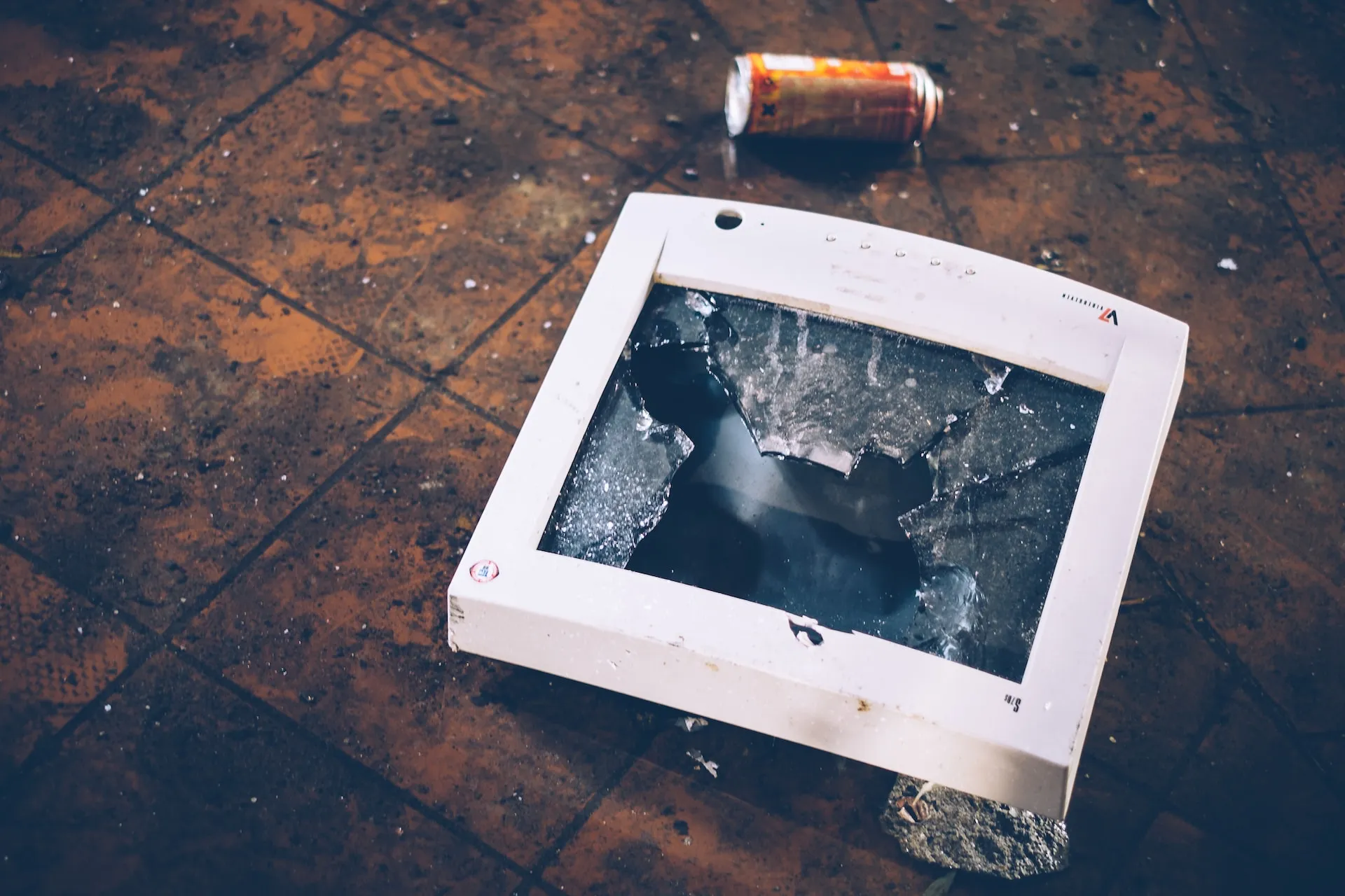 A destroyed monitor on the sidewalk with a crushed soda can